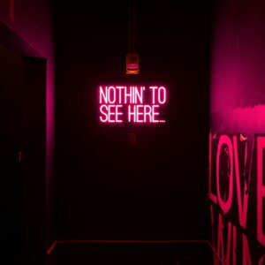 Neon sign reading 'Nothin' to see here...' in an artistic dark room.