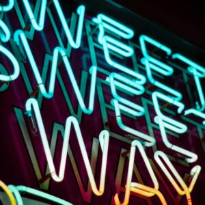 Close-up of colorful neon sign spelling 'Sweet Sweet Way' on a dark background.